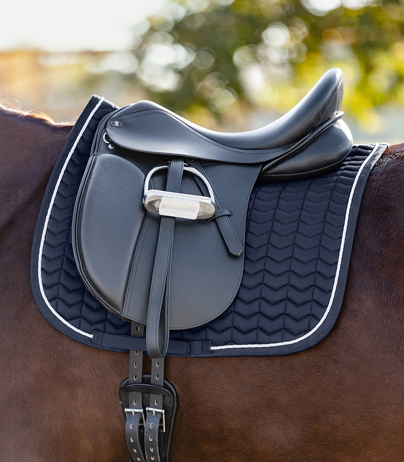 Tapis bleu élégant avec surpiqûres originales en forme de chevrons, fixé sous une selle d'équitation noire sur un cheval.
