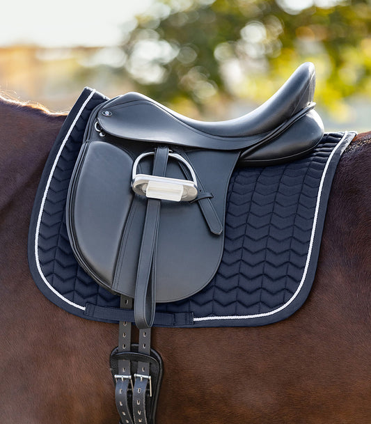 Tapis bleu élégant avec surpiqûres originales en forme de chevrons, fixé sous une selle d'équitation noire sur un cheval.
